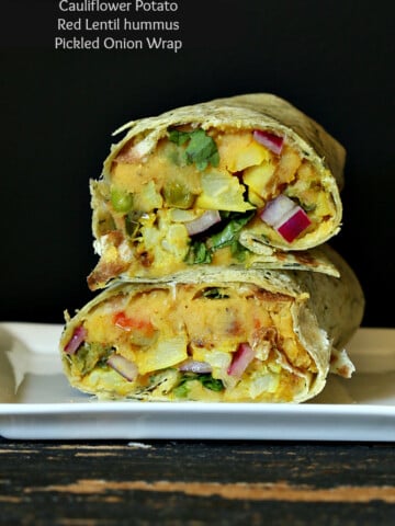 a stacked red lentil hummus wrap against a black background