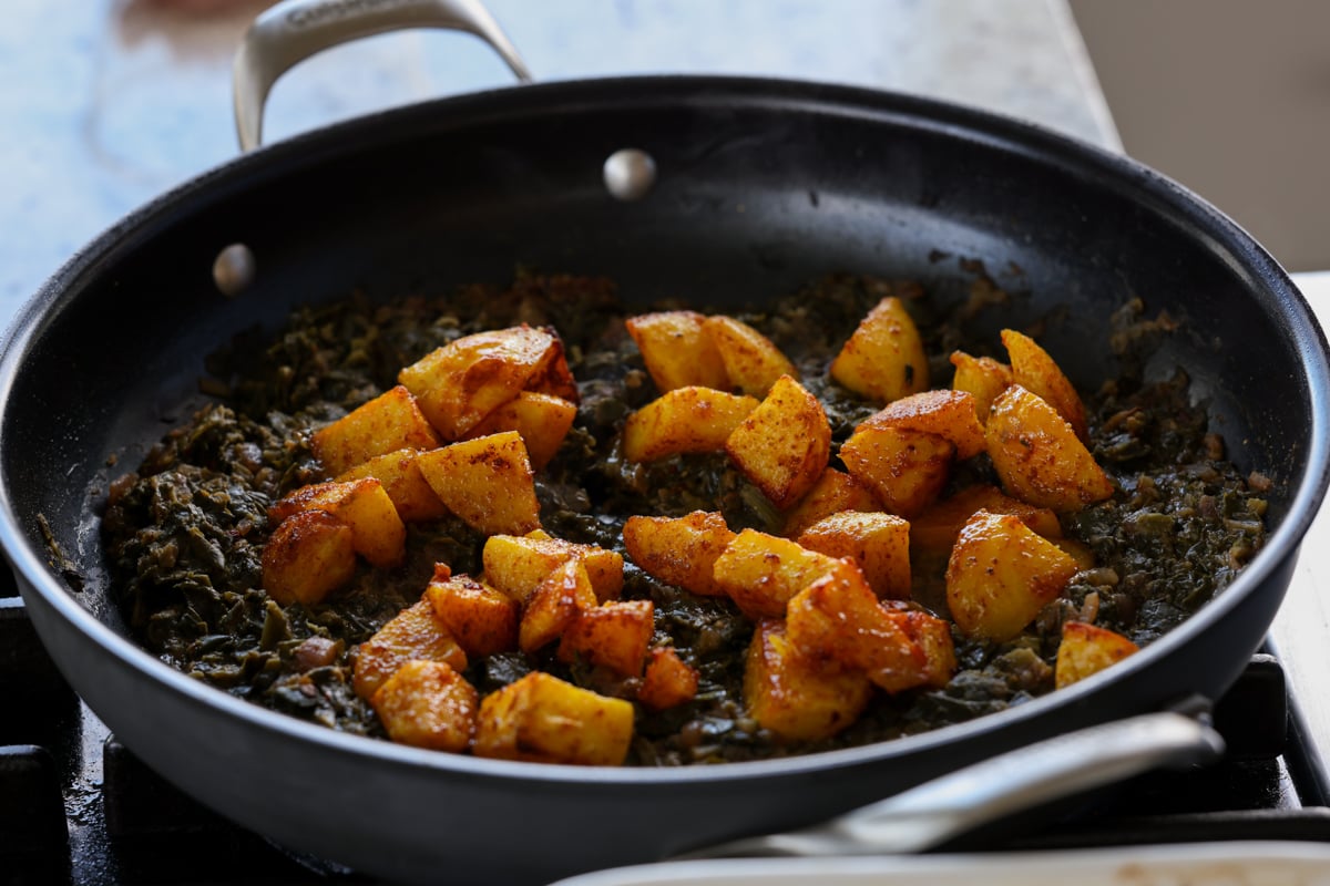 adding potatoes to the pan of saag