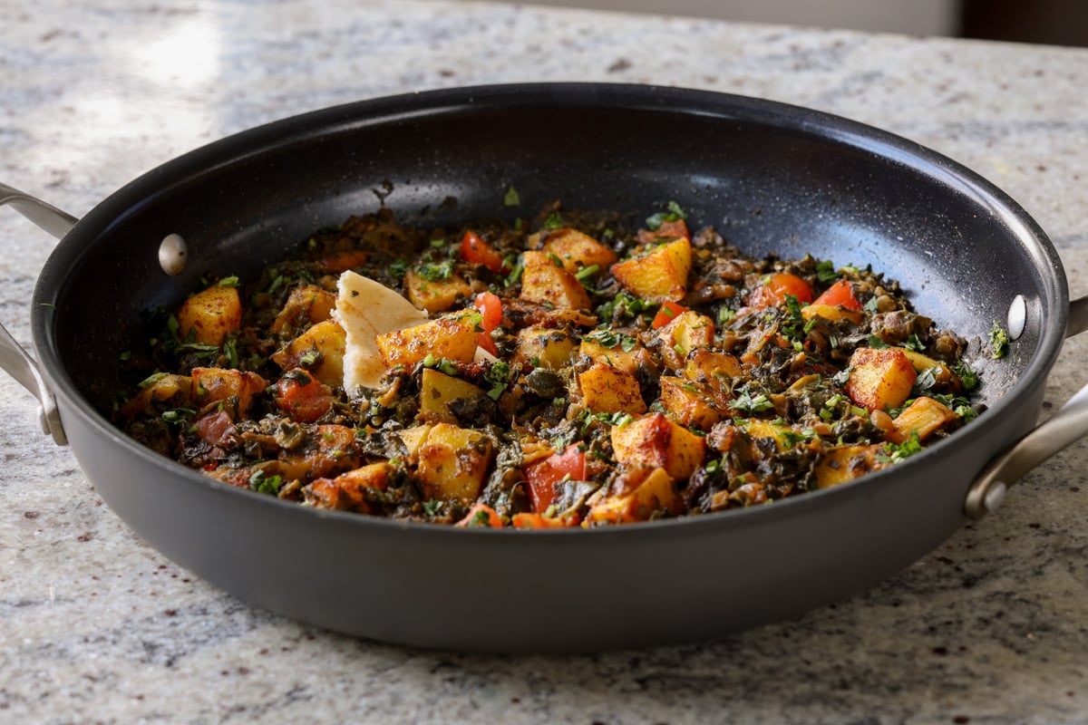 saag aloo in the pan with a piece of flatbread