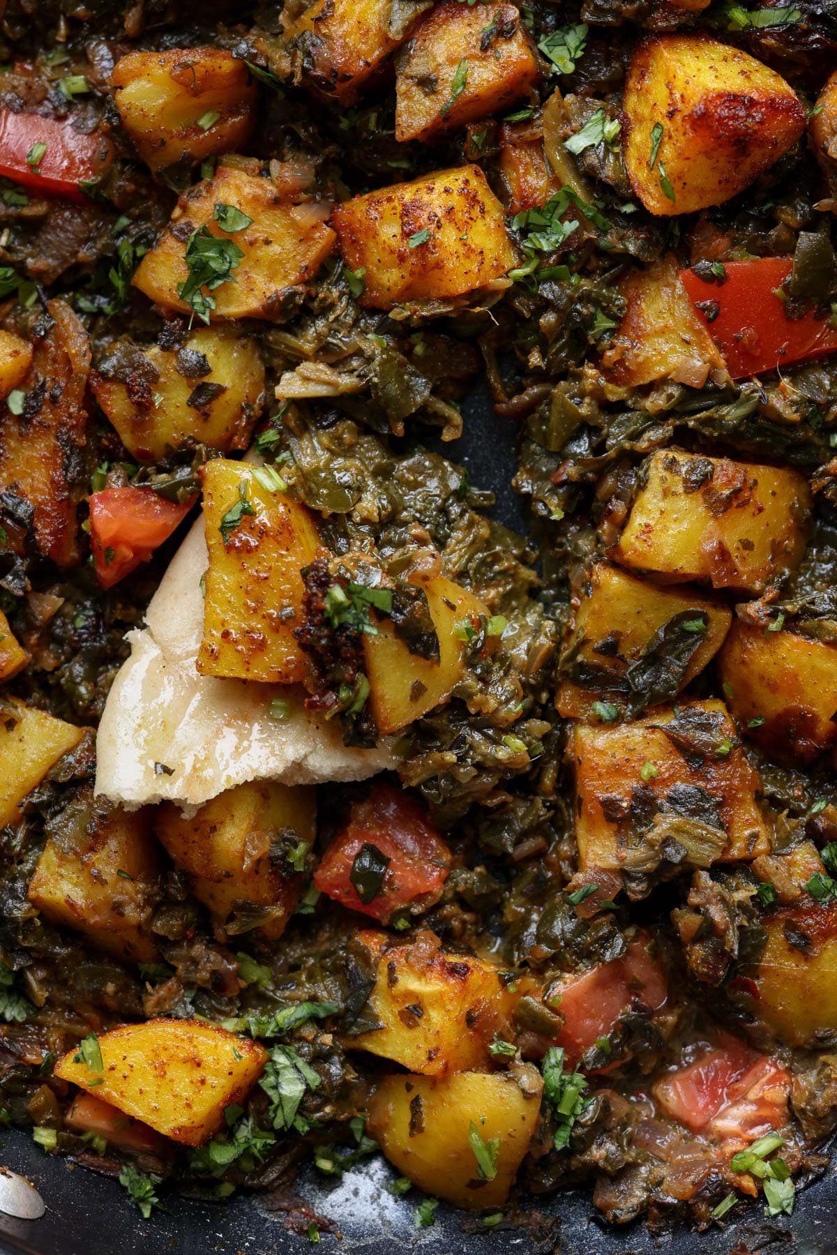 close-up of saag aloo in the pan with a piece of flatbread