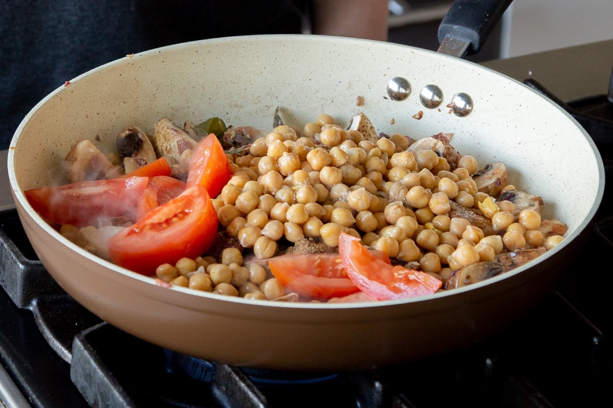 adding chickpeas and tomato pieces to the pan