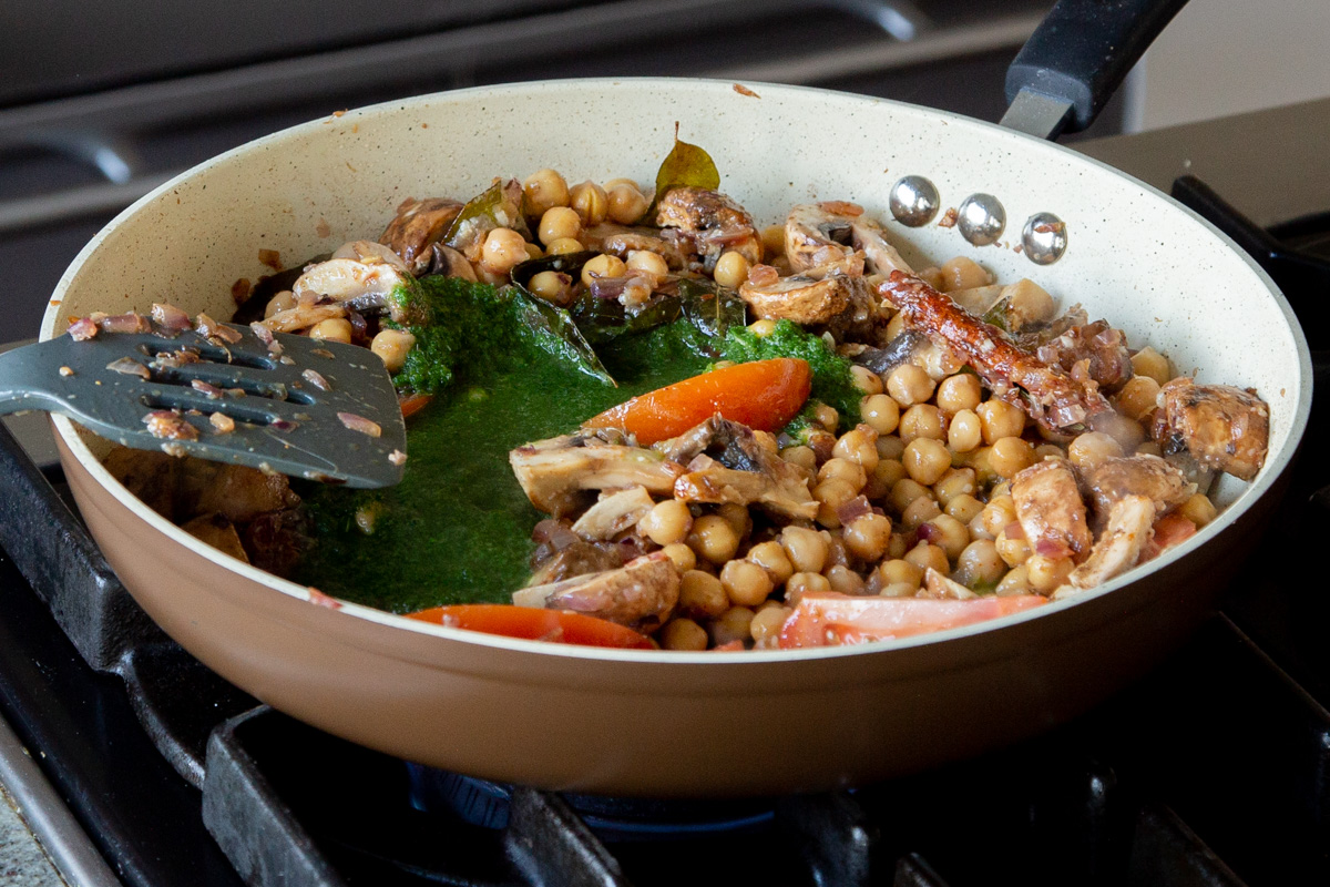 adding the green sauce to the pan of chickpea and veggies