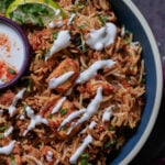 Lucknowi biryani in a bowl topped with raita