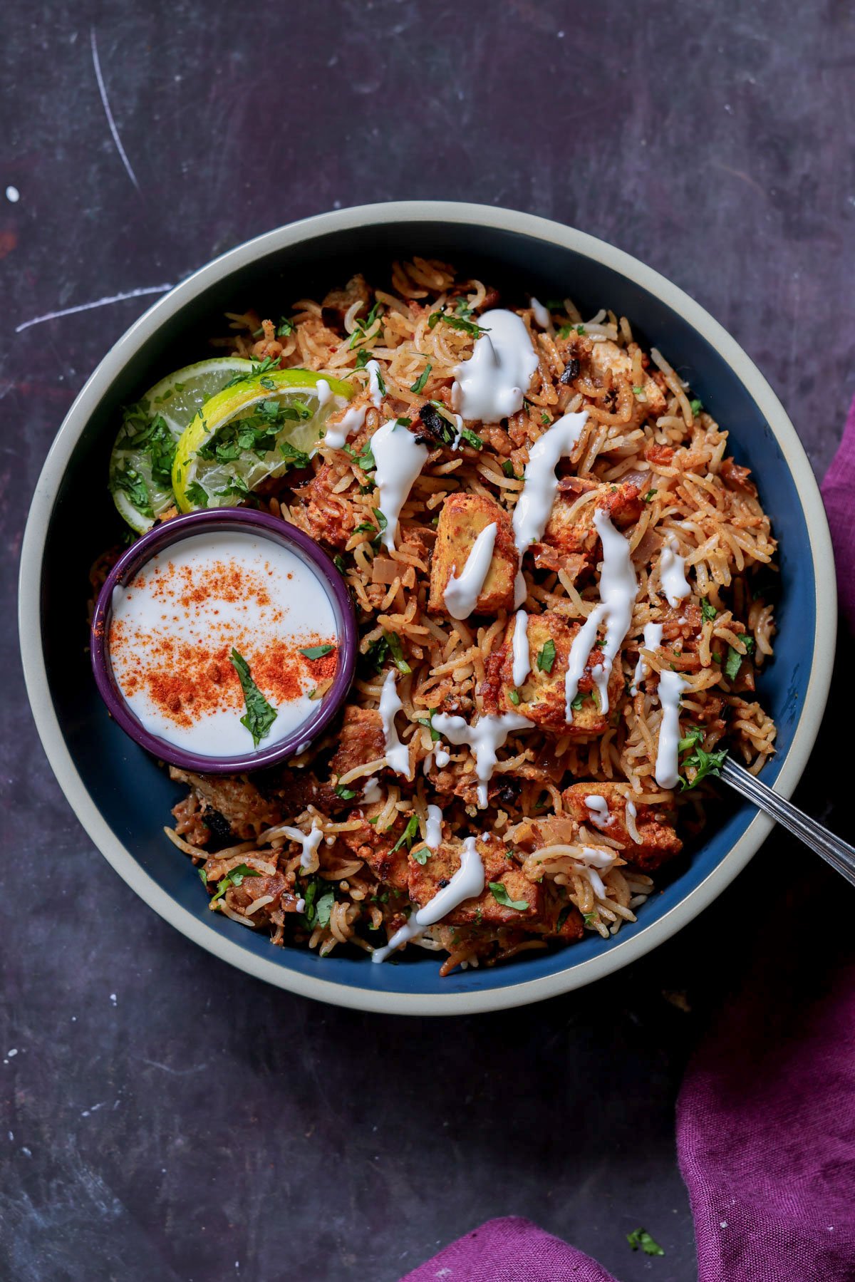 Lucknowi biryani in a bowl topped with raita and a ramekin of raita on the side