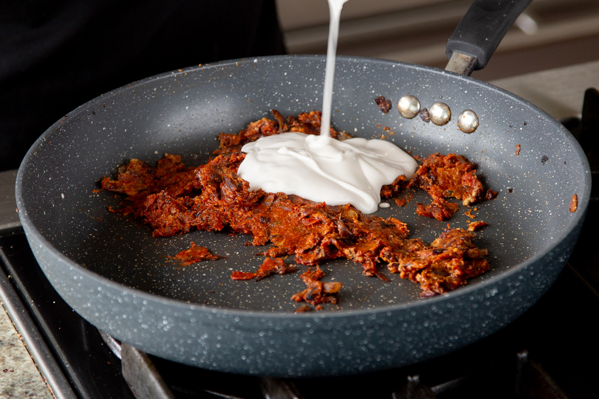 adding non-dairy yogurt to the pan of spiced onions