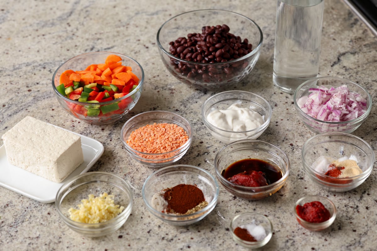 tofu, beans, spices, and other burrito bowl ingredients in bowls on a kitchen counter