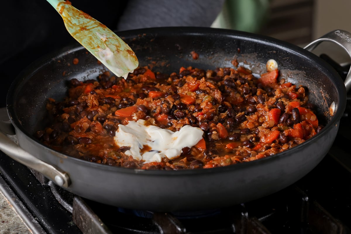 adding vegan sour cream to the cooked beans in the pan