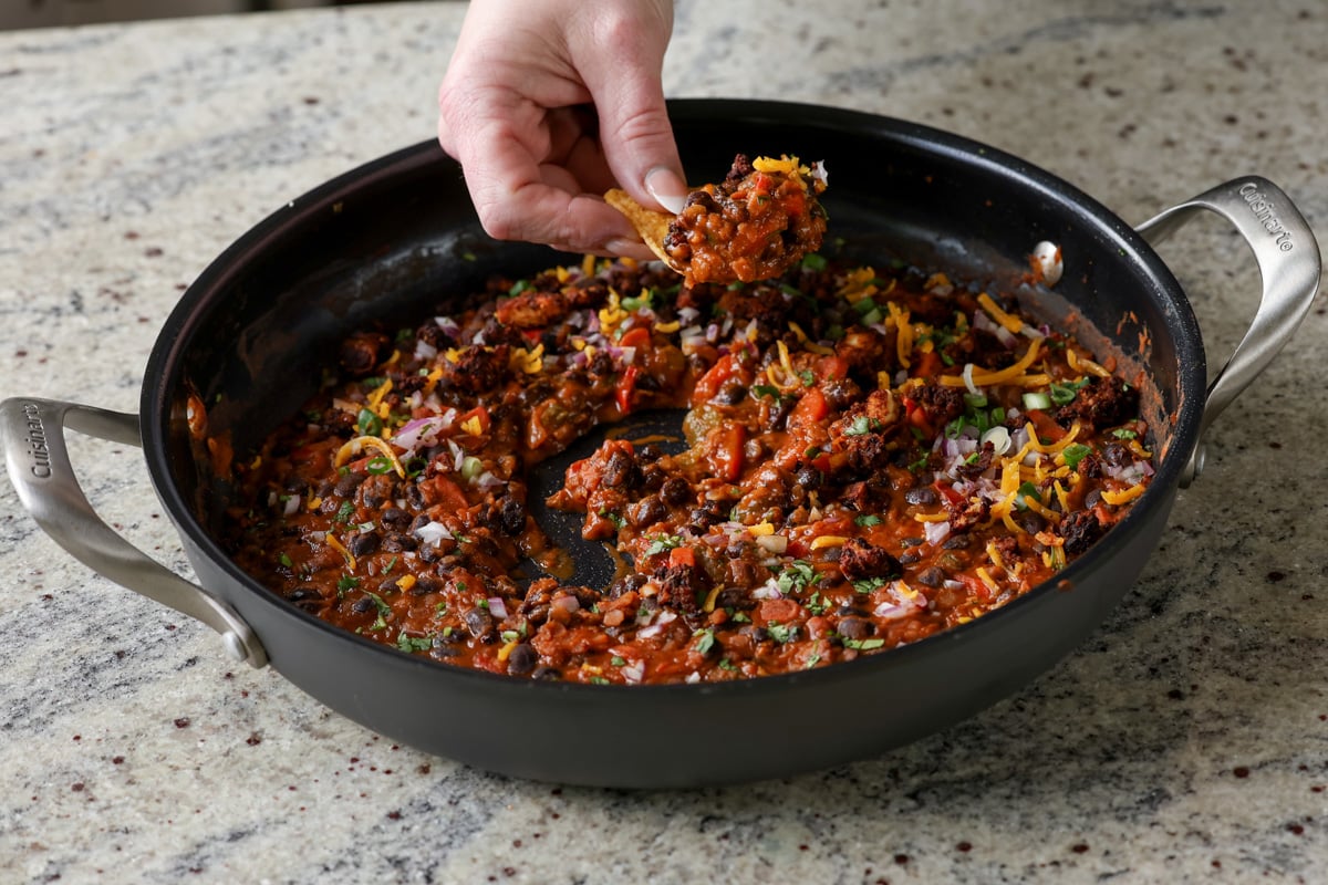 dipping a tortilla chip into the pan of black beans and lentils