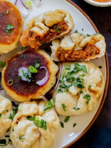 serving plate of butter chicken bao with one flipped so you can see the crispy bottom and one town in half so you can see the filling