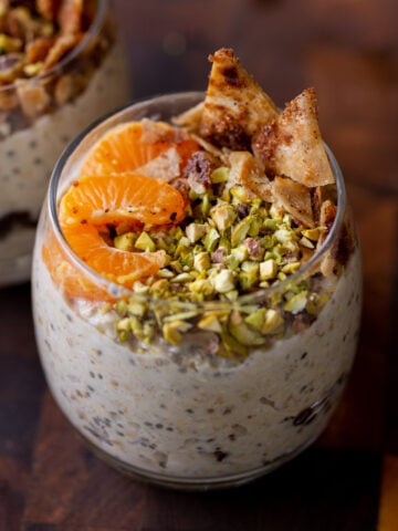 cannoli overnight oats in a glass topped with oranges, pistachios, and crispy cinnamon sugar tortilla pieces