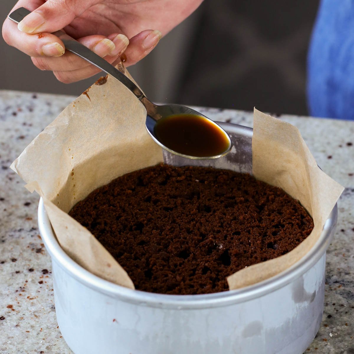 spooning coffee syrup onto the second layer of mocha cake
