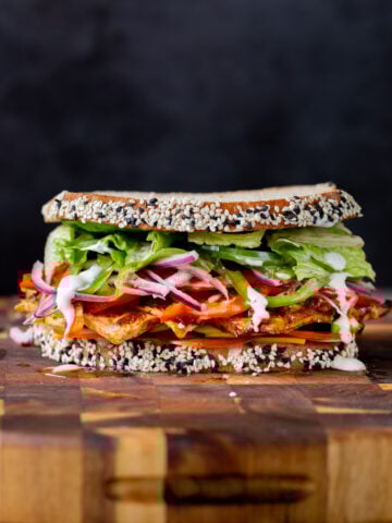 vegan club sandwich with veggies and tofu deli meat on a wooden cutting board