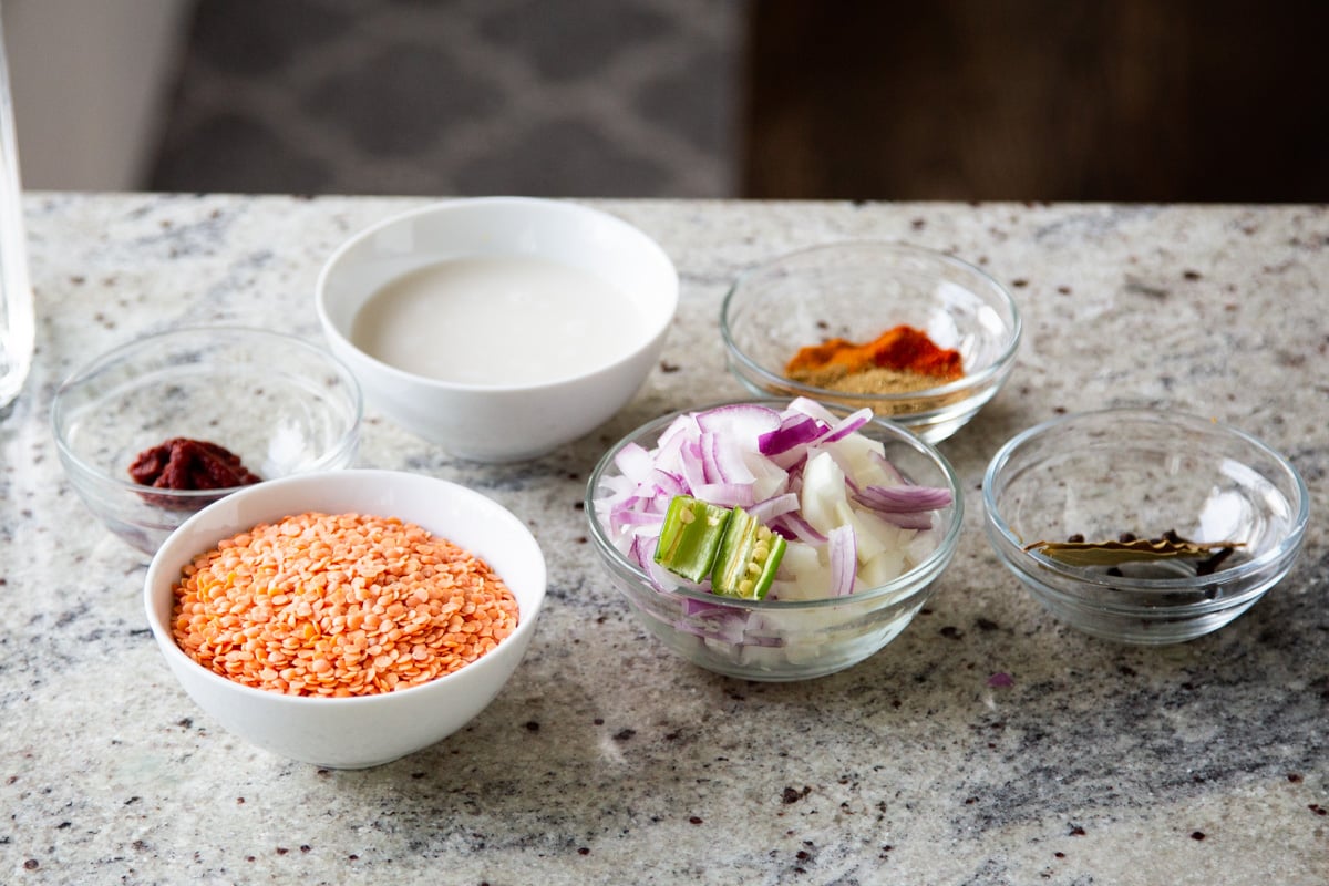 lentils, veggies, spices, and other dalcha ingredients in bowls on a kitchen counter