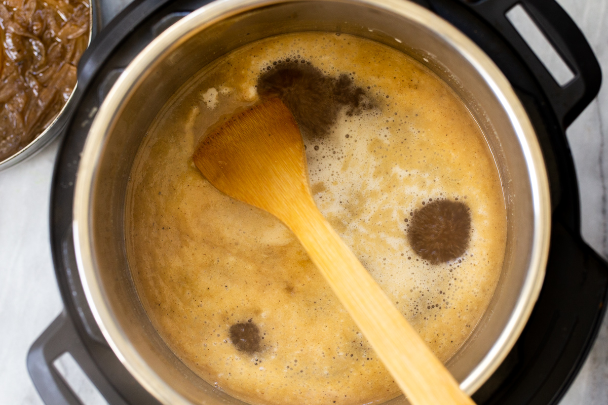vegan French Onion soup being stirred in an Instant Pot with a wooden spoon 