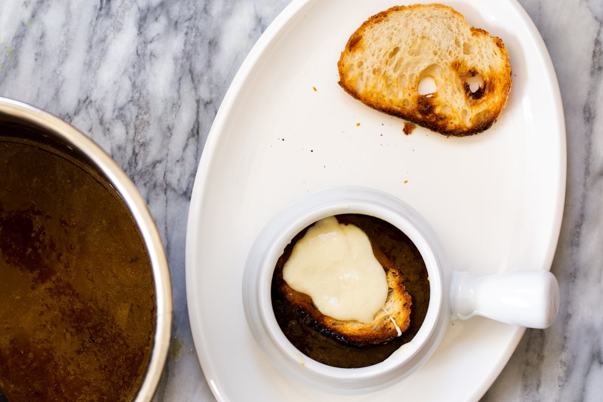 a small serving of vegan French Onion Soup topped with a slice of sourdough topped with liquid mozzarella