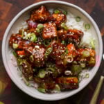 General Tso's tofu in a bowl with green onion and sesame seeds
