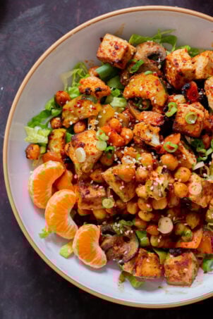 close-up of gochujang tofu and veggies in bowl over lettuce with orange pieces and sesame seeds