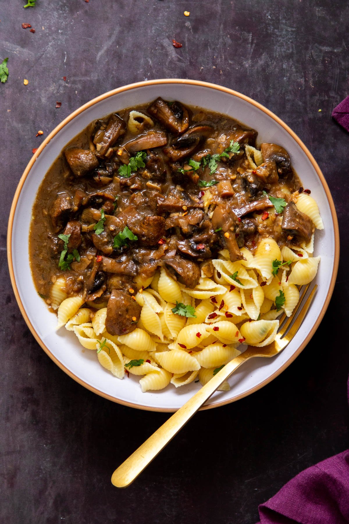 a white bowl with garlic mushrooms and pasta with a golden fork on the side