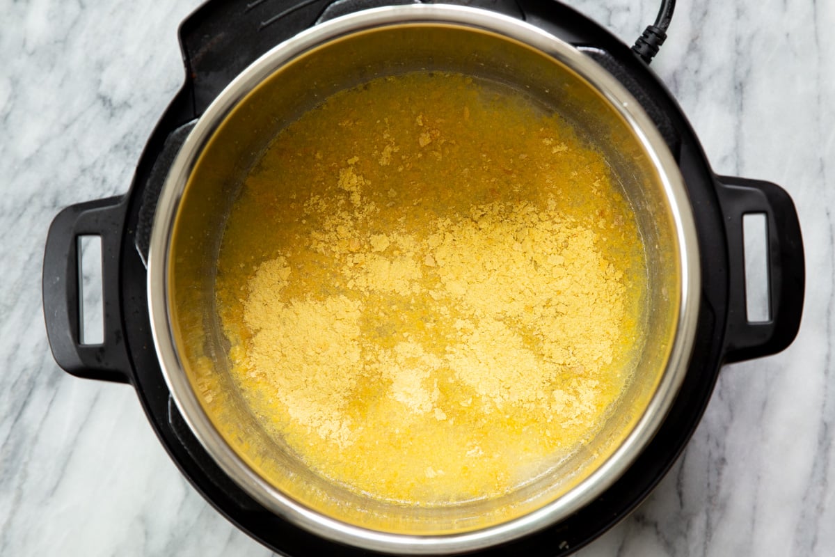 Nutritional yeast being added to an instant pot with ingredients for vegan cheese sauce 