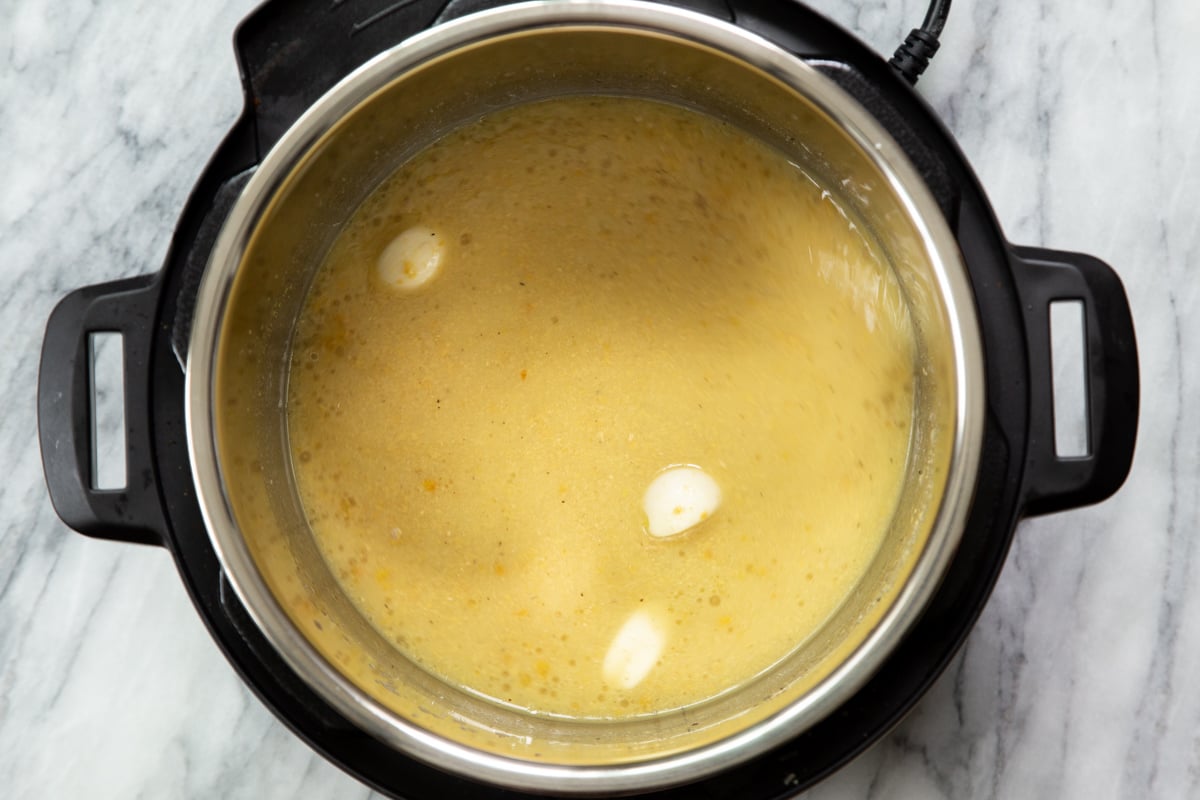 garlic being added to instant pot with vegan cheese sauce ingredients