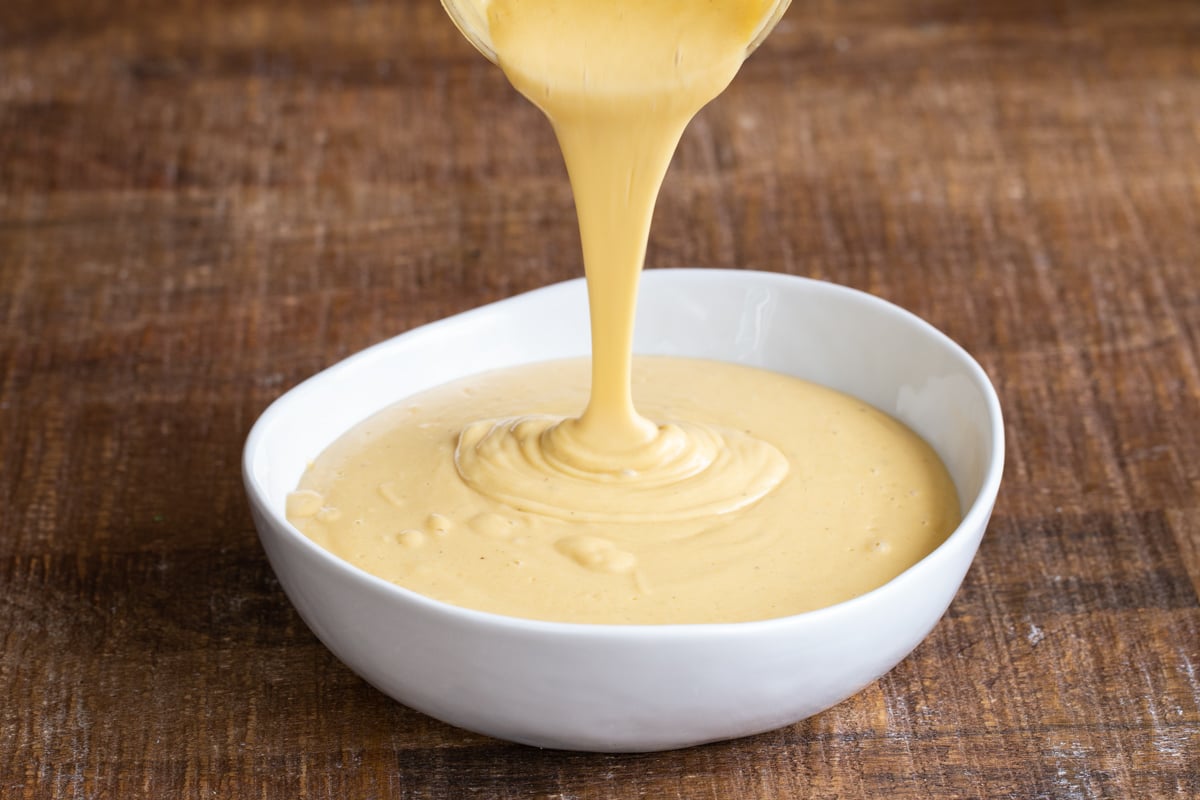 blended vegan cheese sauce being poured into a small white dish