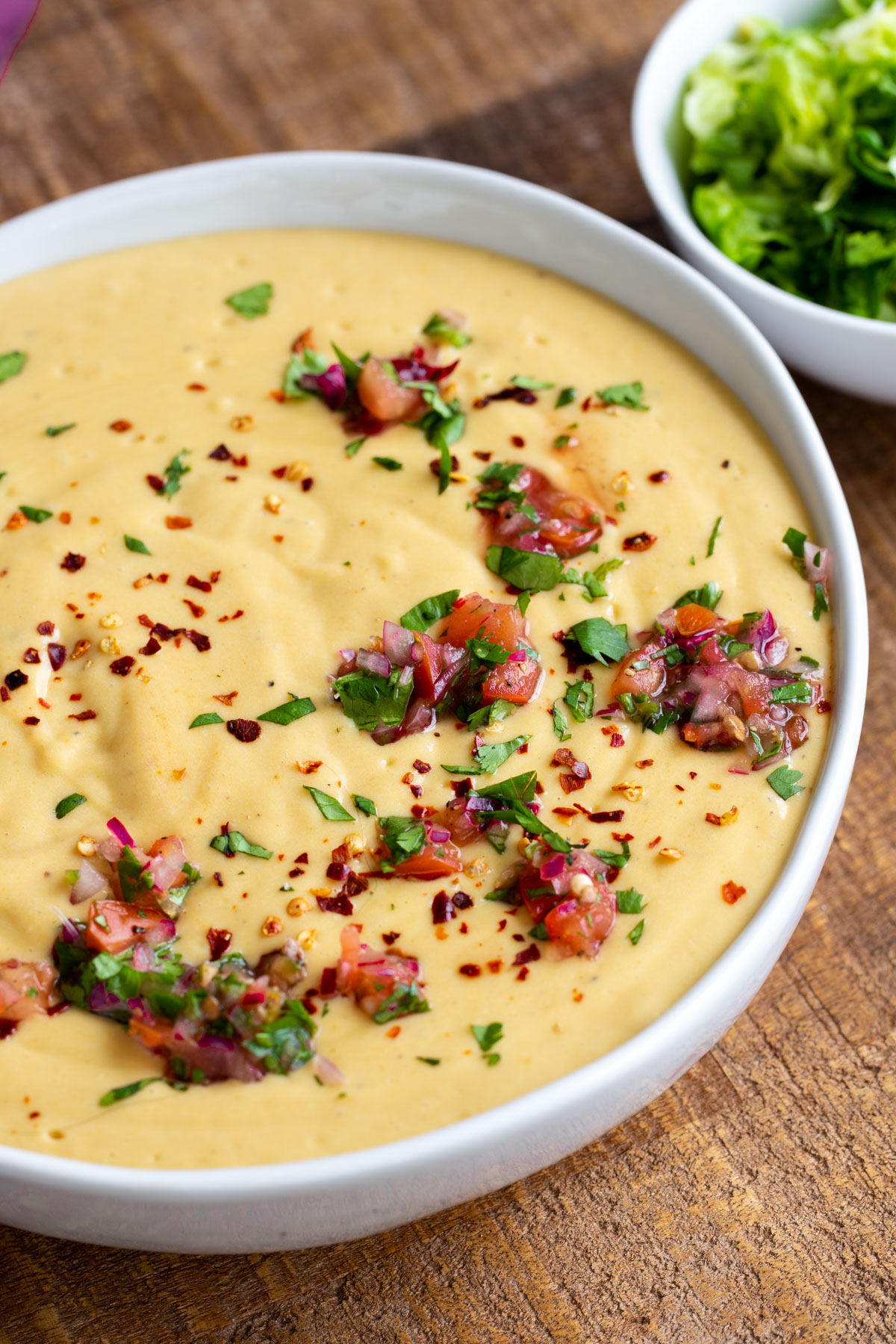 a white bowl filled with Instant Pot Vegan Cheese Sauce decorated with fresh chopped herbs and tomatoes 