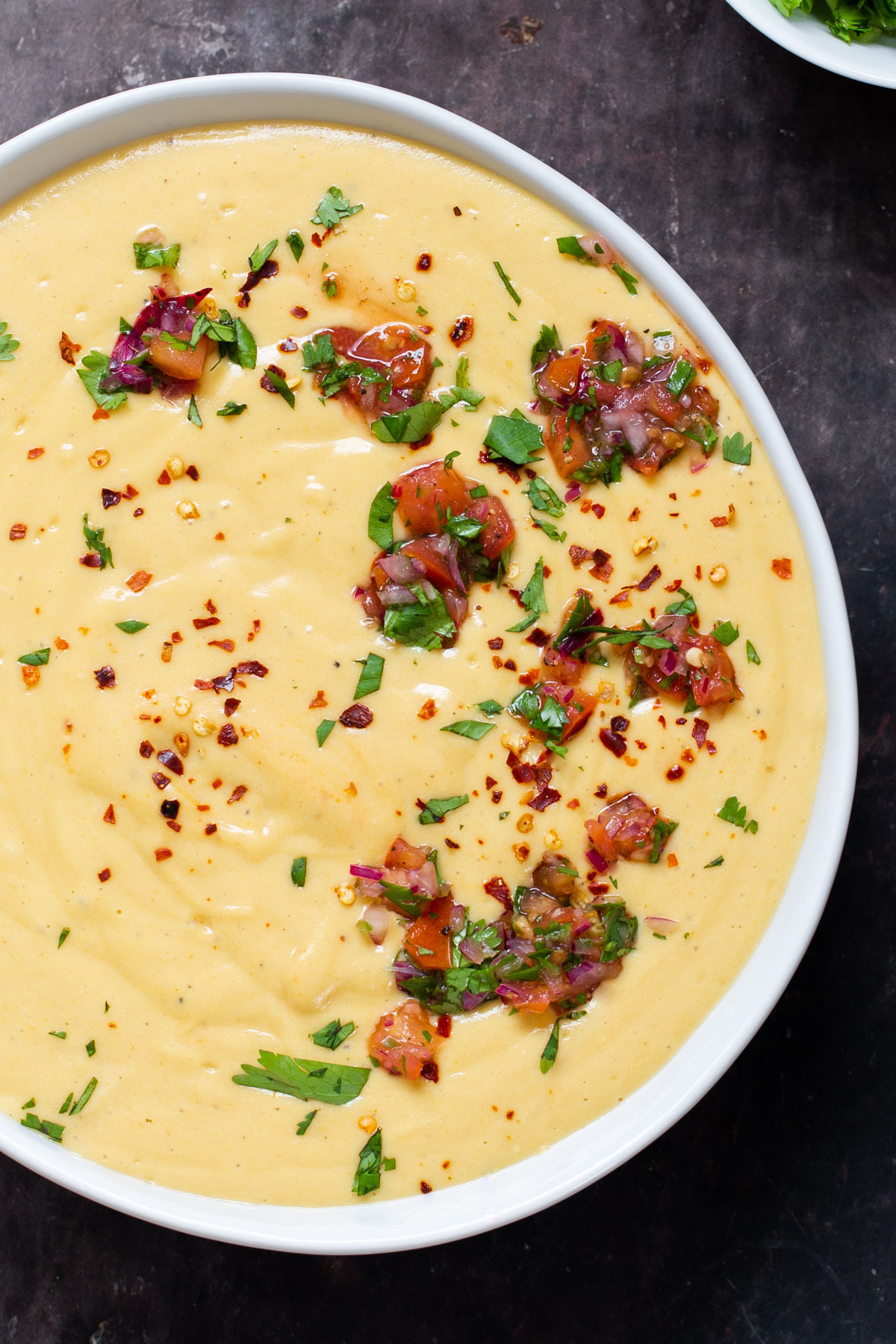 overhead shot of a bowl of vegan cheese sauce sprinkled with chopped herbs and tomatoes 