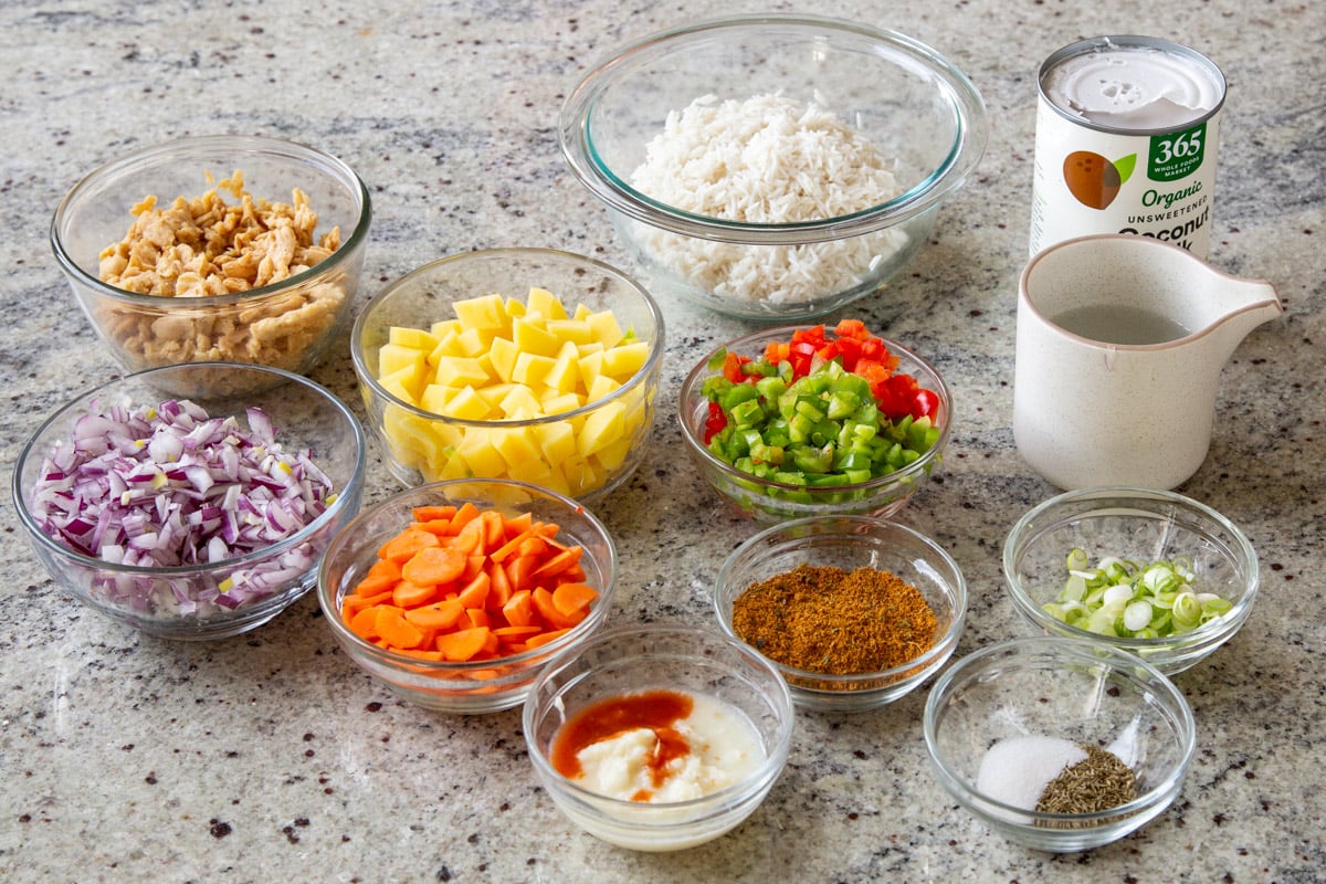 rice, potatoes, Jamaican curry powder, and other ingredients in bowls on a kitchen counter