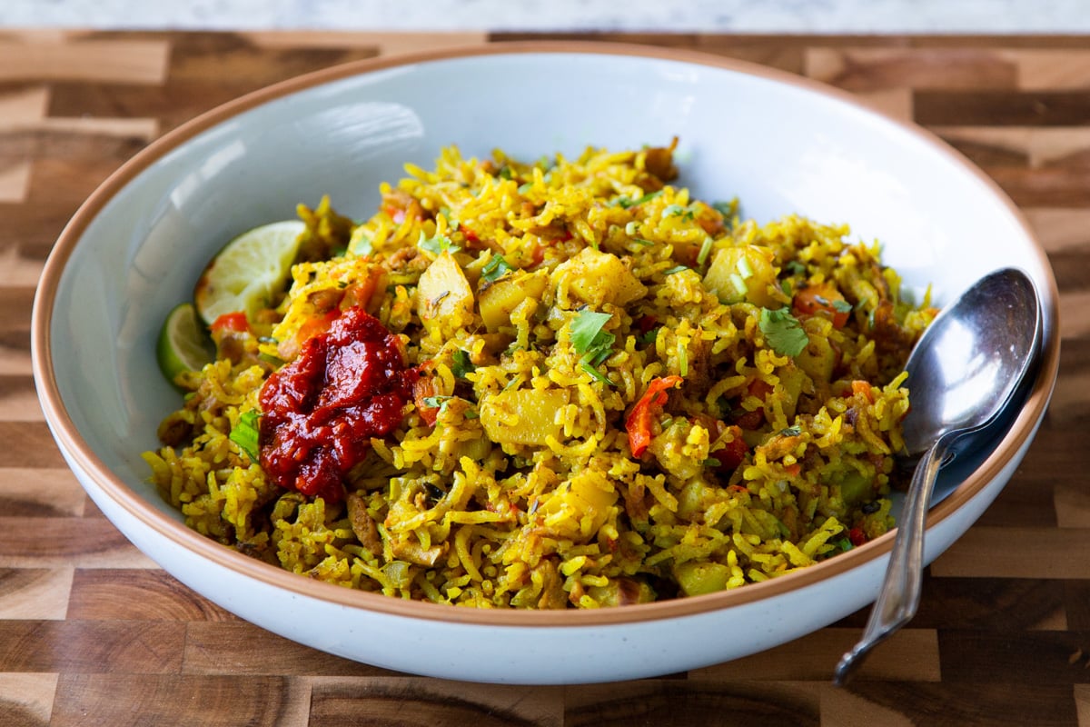bowl of Jamaican curry rice with hot sauce and lime