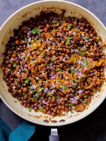 ghugni garnished with onions, cilantro, and cumin in the frying pan