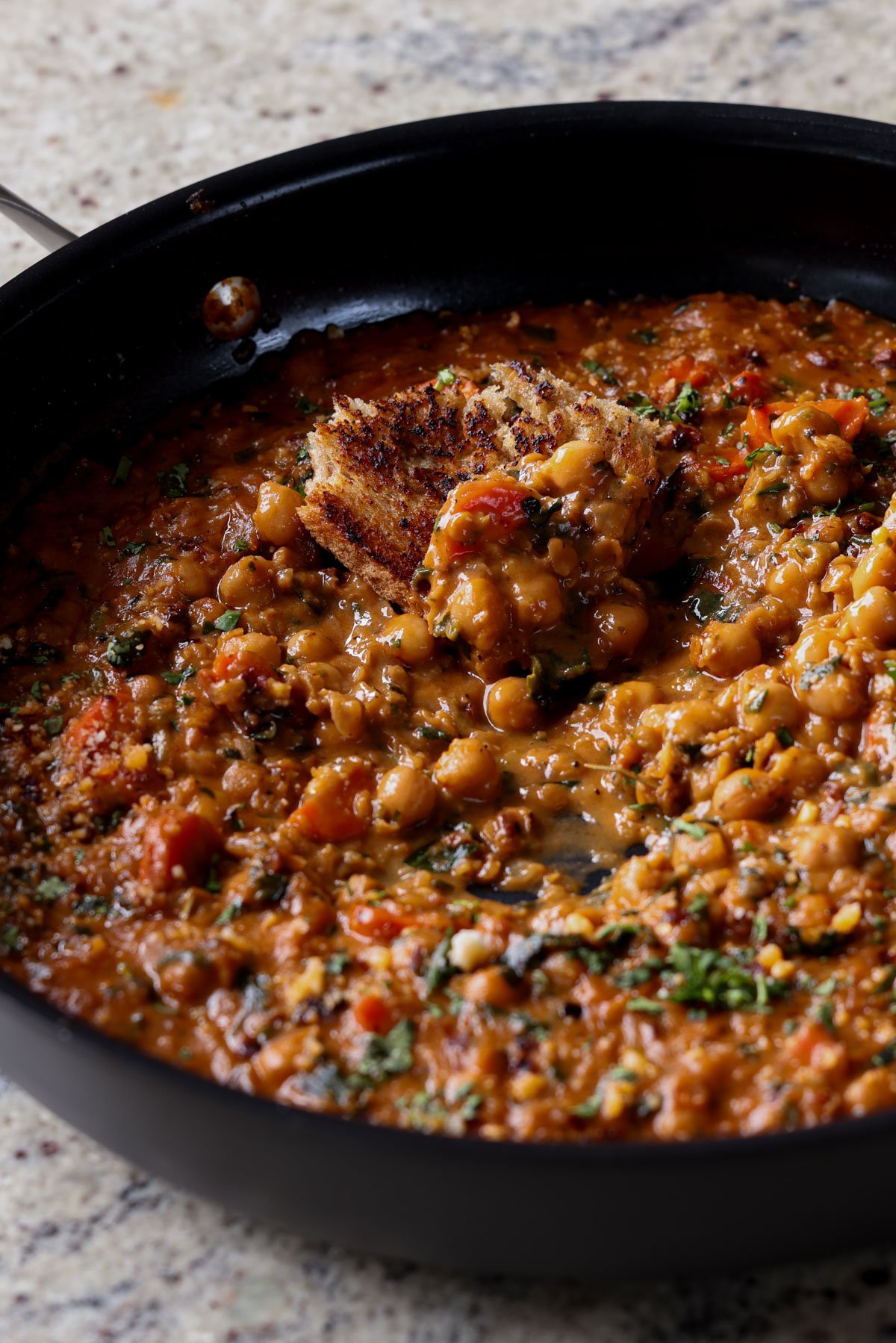 piece of toast in the pan of lentil chickpea stew