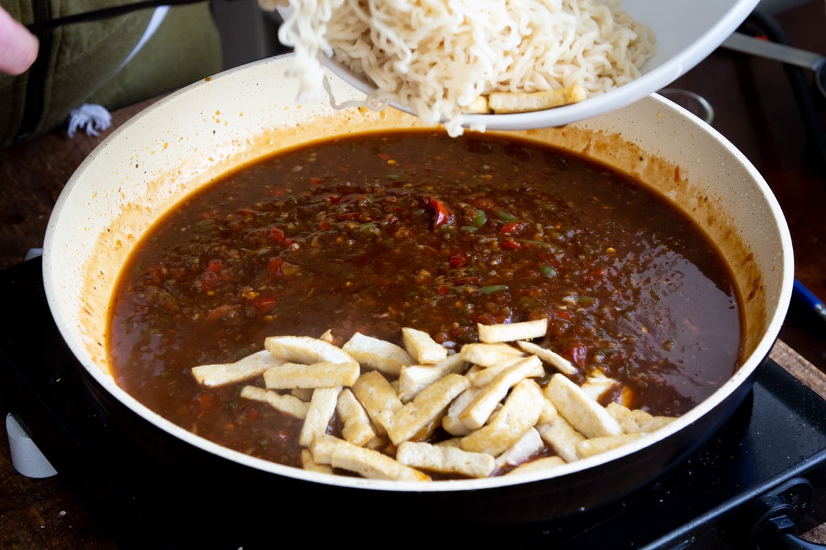 noodles and fried tofu being added to a saucepan with Manchurian Sauce