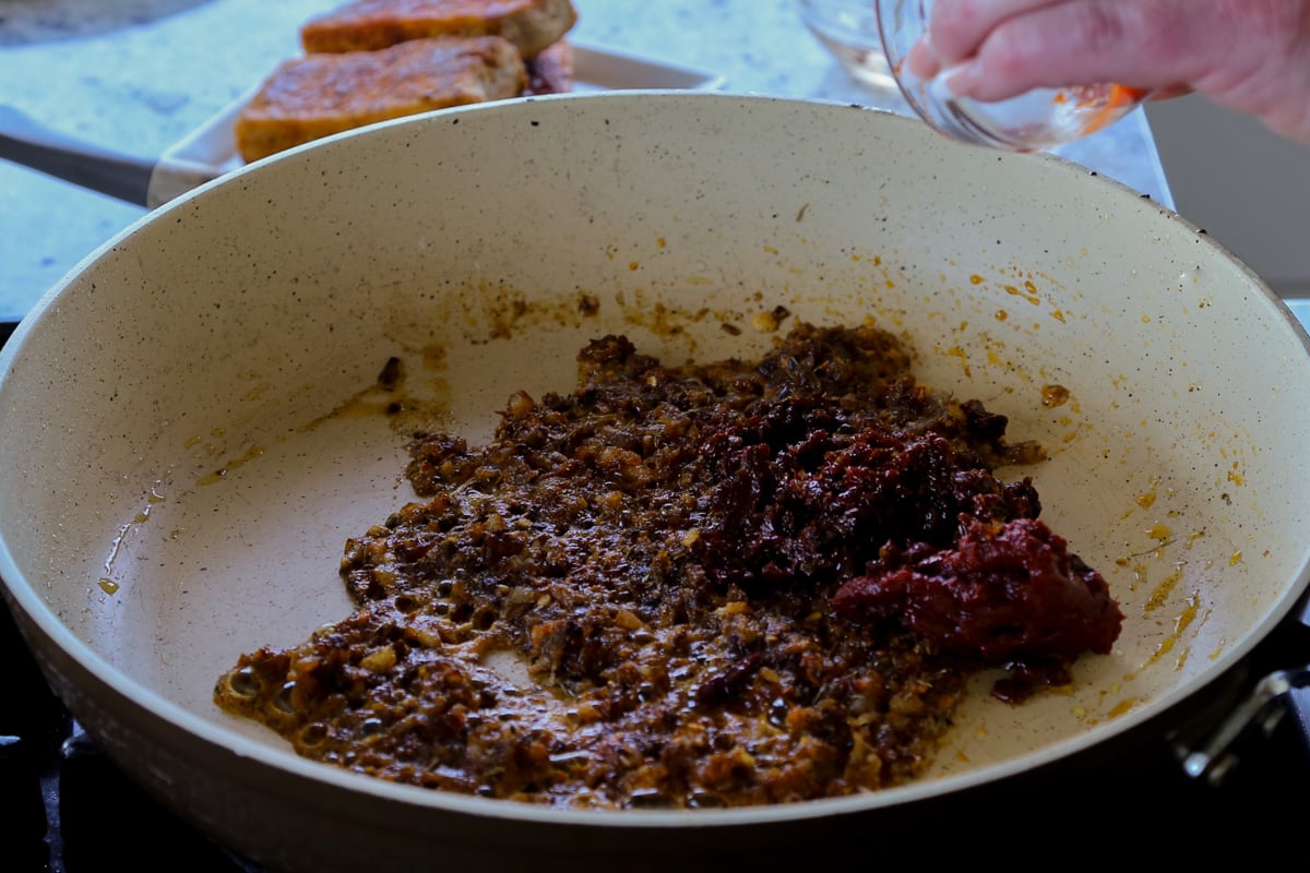 adding tomato paste to the pan with the onion and spices