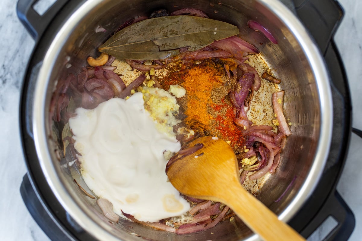 ground spices and yogurt being added to an Instant Pot with sauteed onion