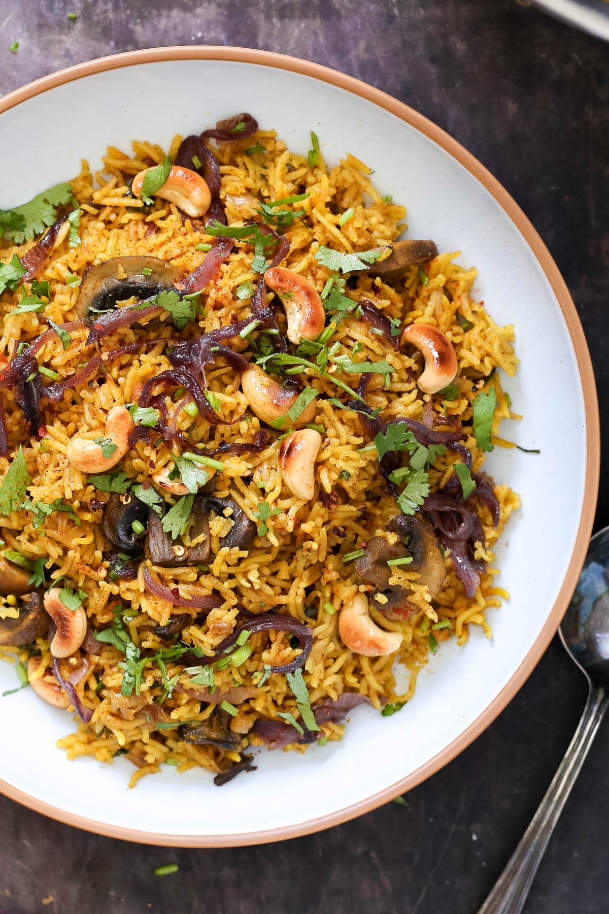 a plate with vegan mushroom biryani topped with toasted cashews and chopped cilantro