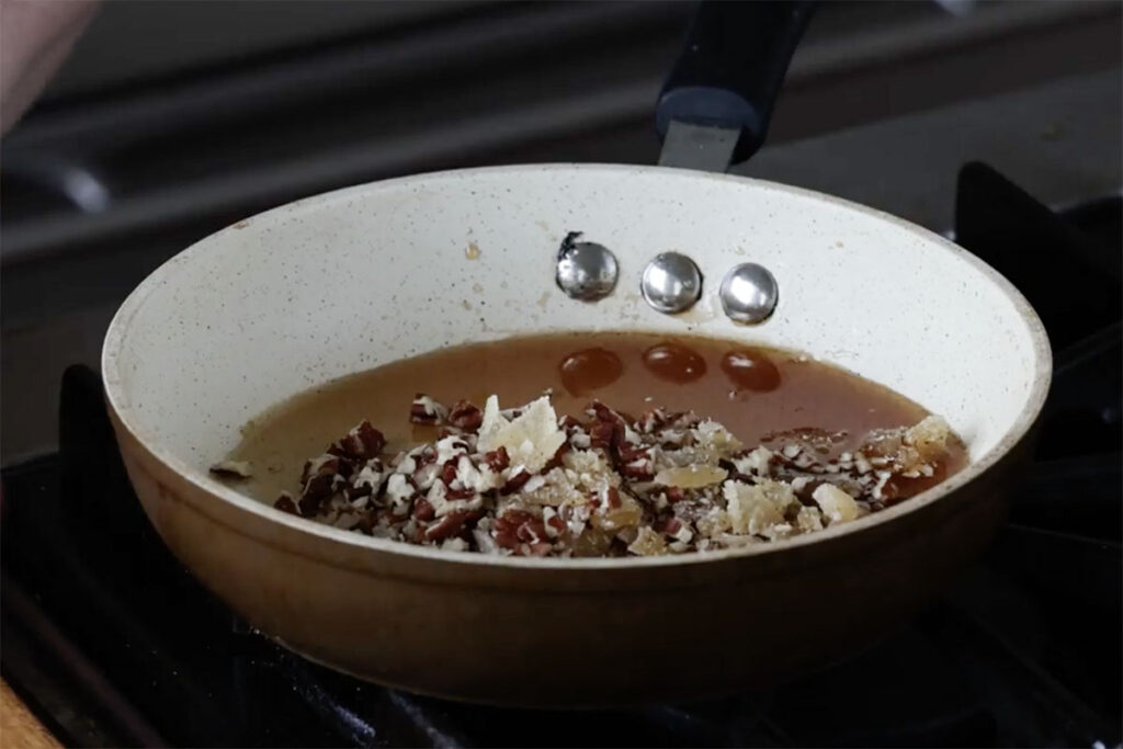adding pecans and candied ginger to the pan of syrup