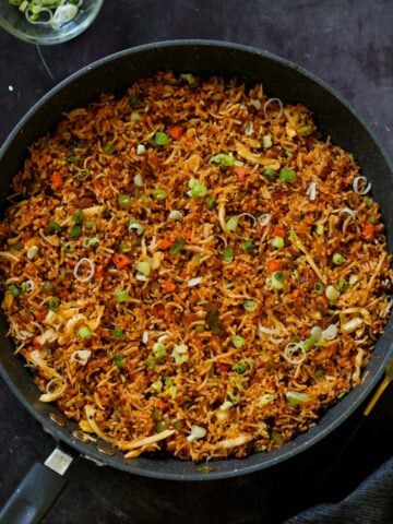Schezwan fried rice in the pan with green onions for garnish