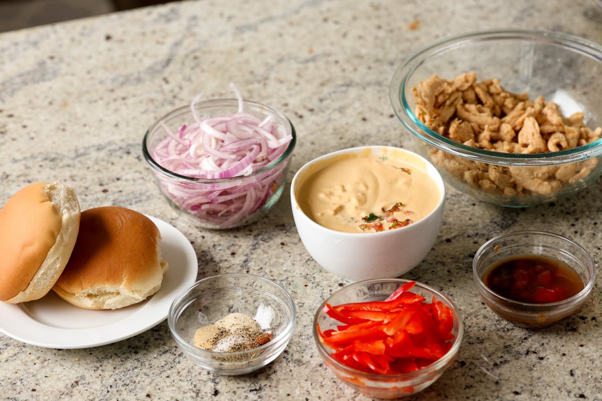 cheese sauce and other vegan cheesesteak ingredients in bowls on a kitchen counter