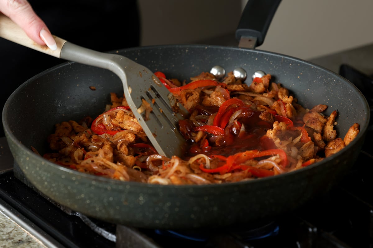 adding sauces to the pan of soy curls, peppers, and onions