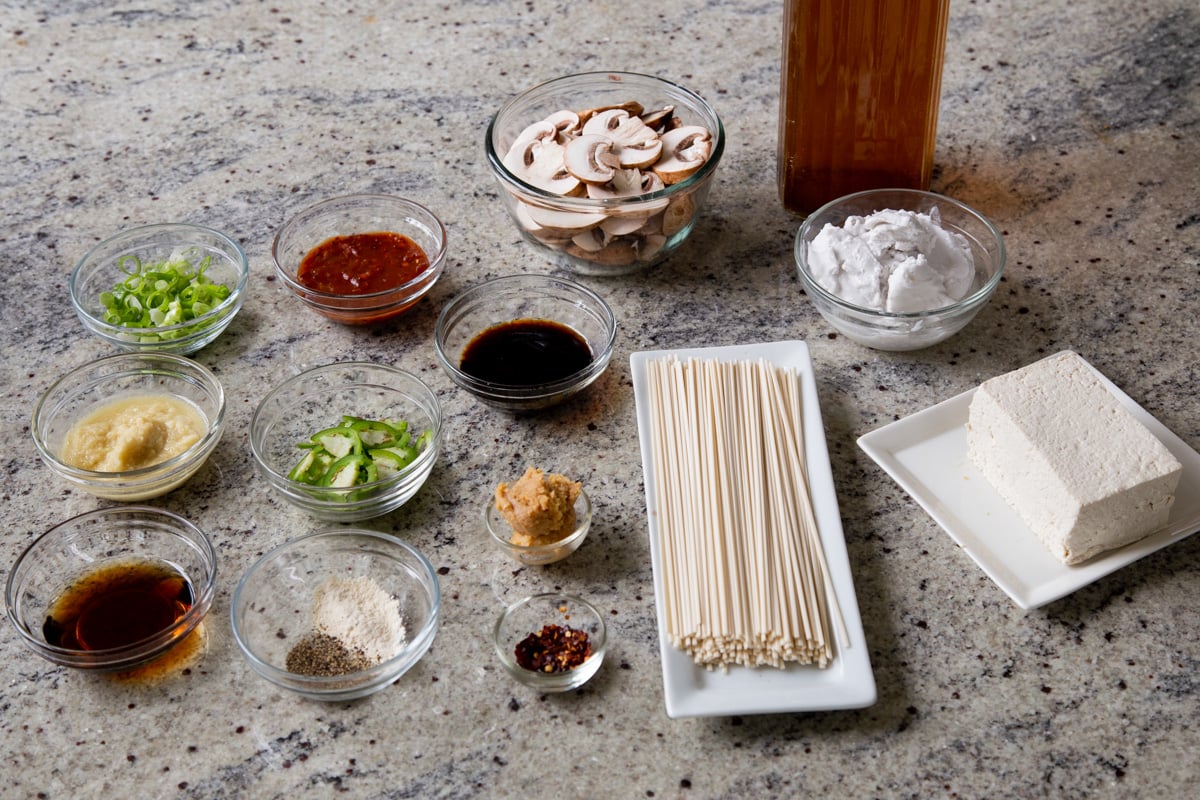 noodles, mushrooms, miso, and other ramen ingredients in bowls on a kitchen counter