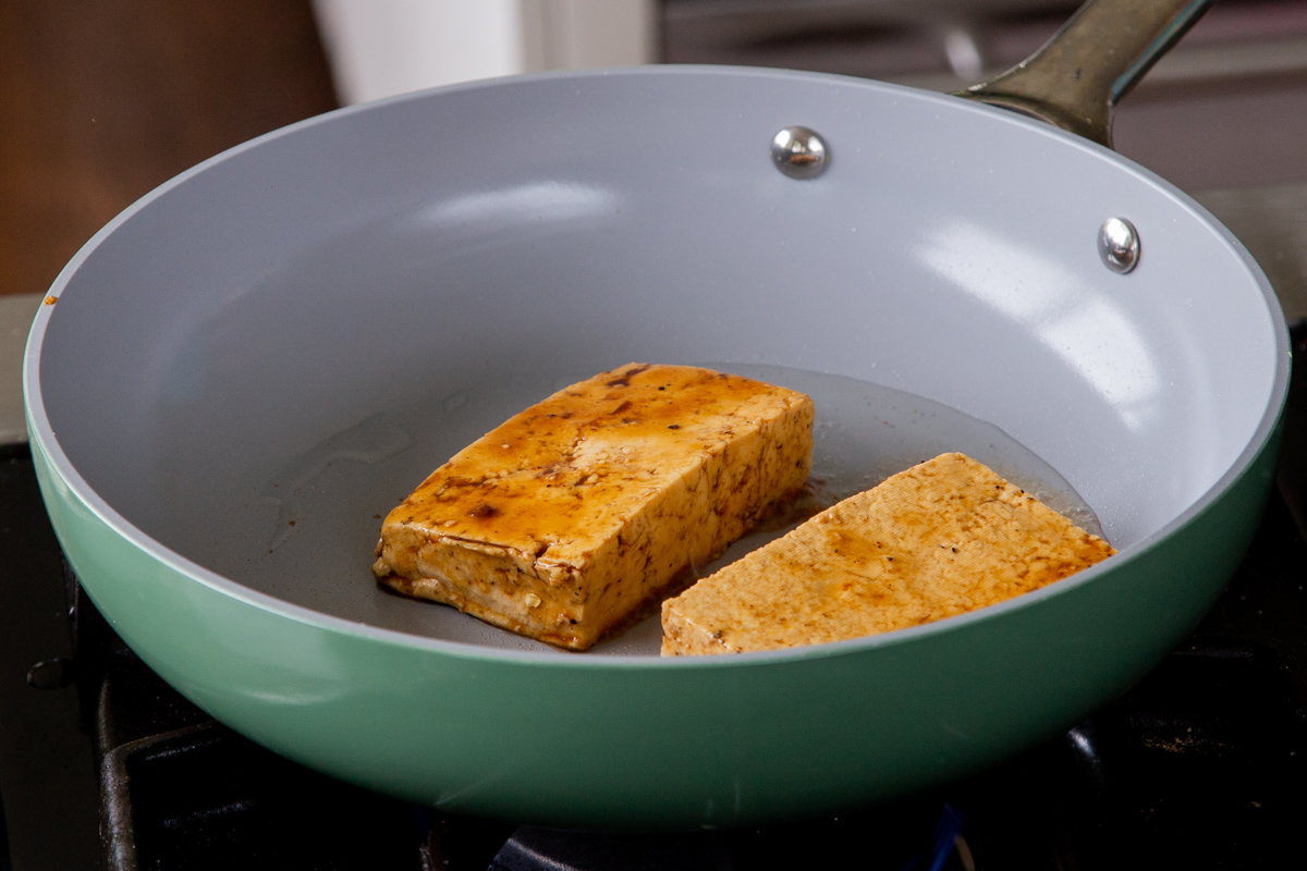 adding marinated tofu slabs to the frying pan