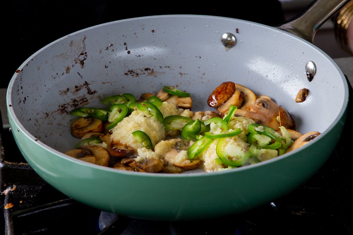 adding ginger-garlic paste and jalapeños to the mushrooms in the frying pan