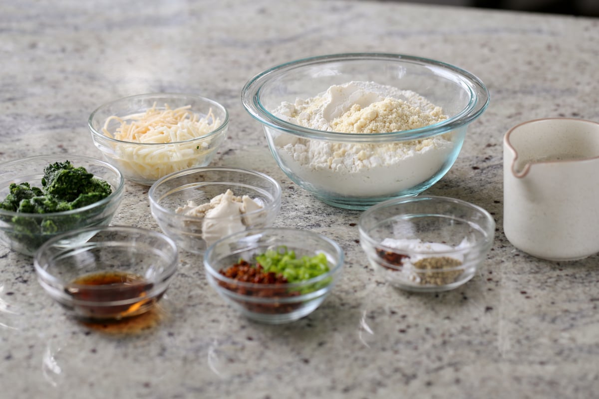 flour, spinach, cheese, and other scones ingredients in bowls on the kitchen counter