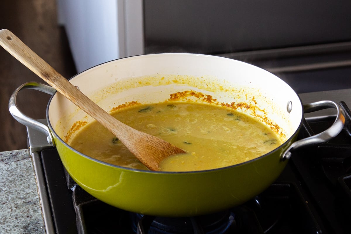 spices and lentils stirred into the water in a green skillet, before cooking