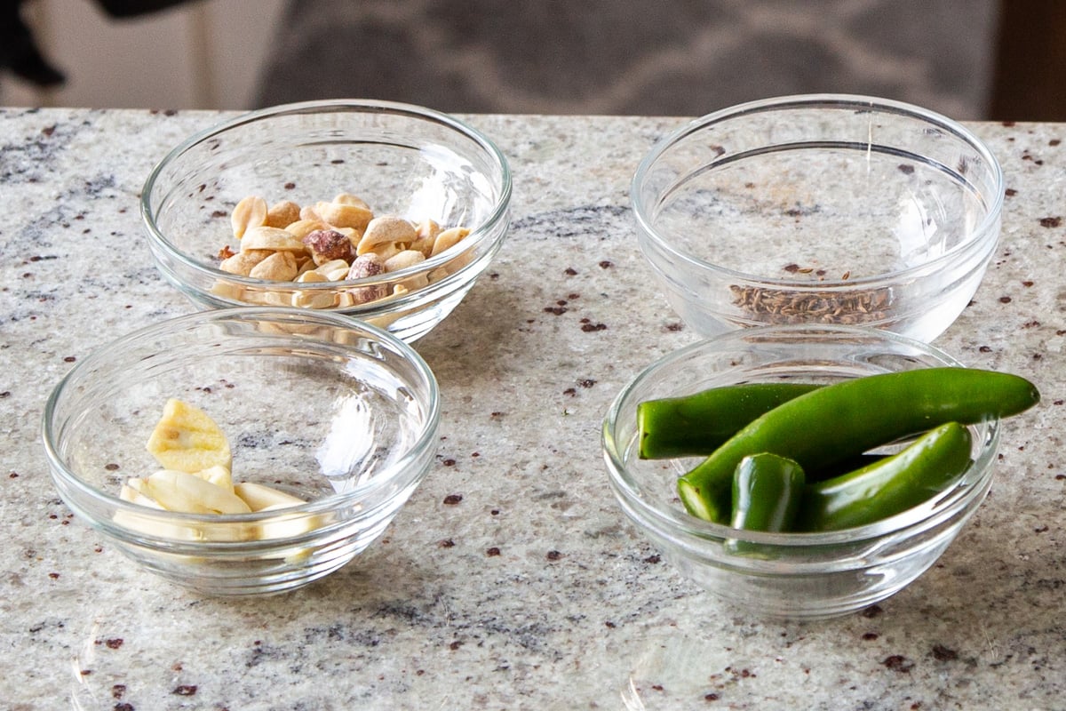 chilis, garlic, peanuts, and cumin seeds in bowls on the kitchen counter