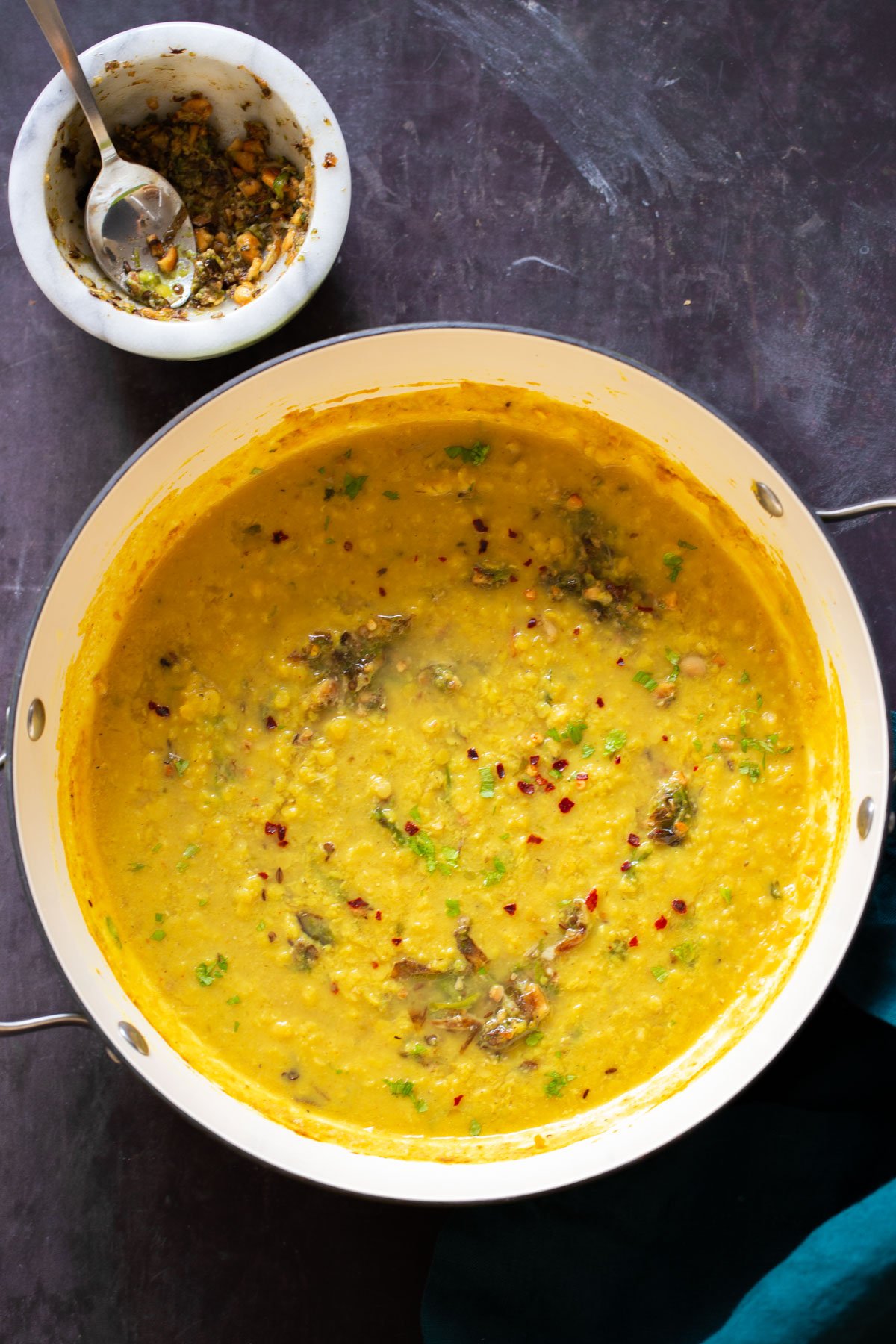 close-up of thecha dal in the skillet next to the mortar of thecha