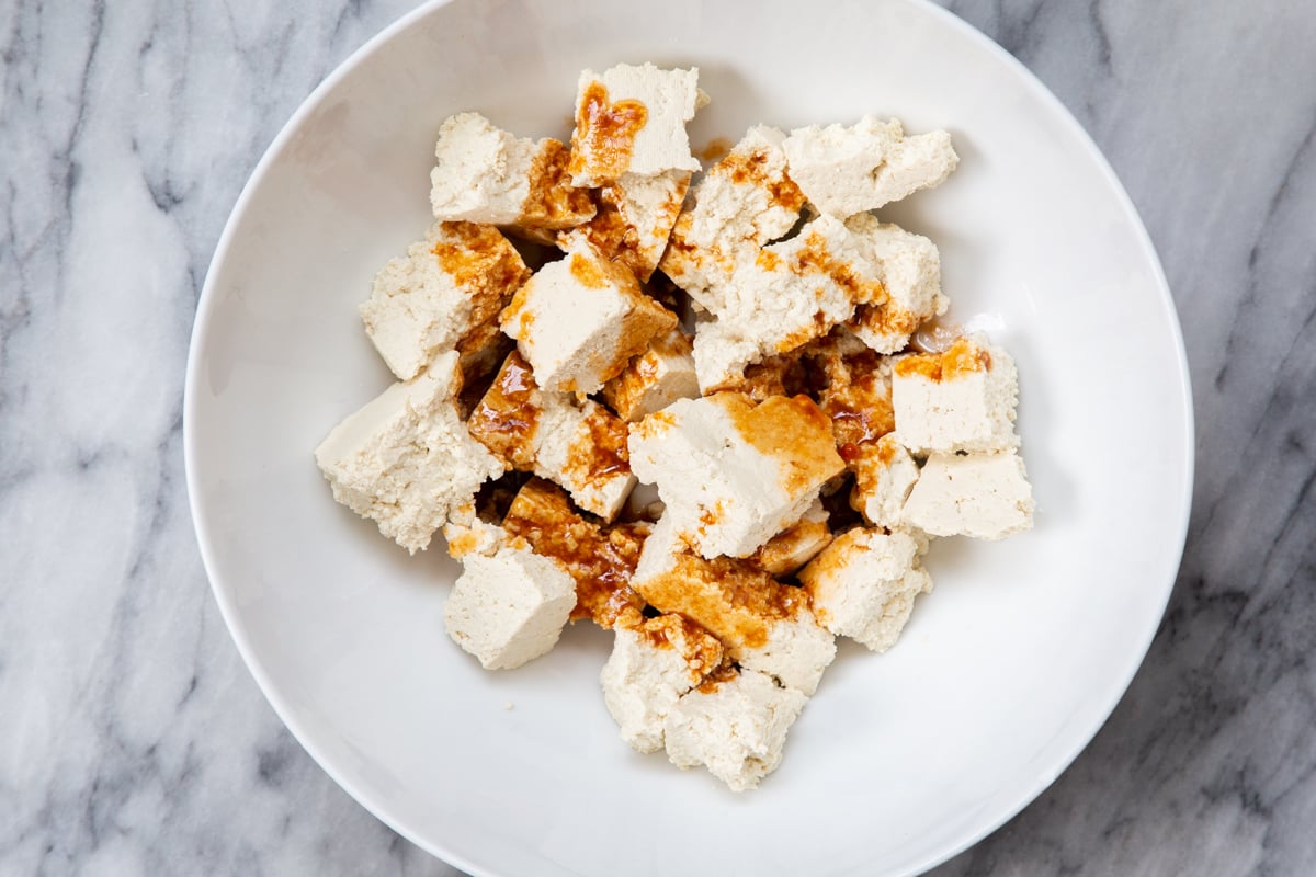 marinade being added to torn tofu chunks in a white bowl