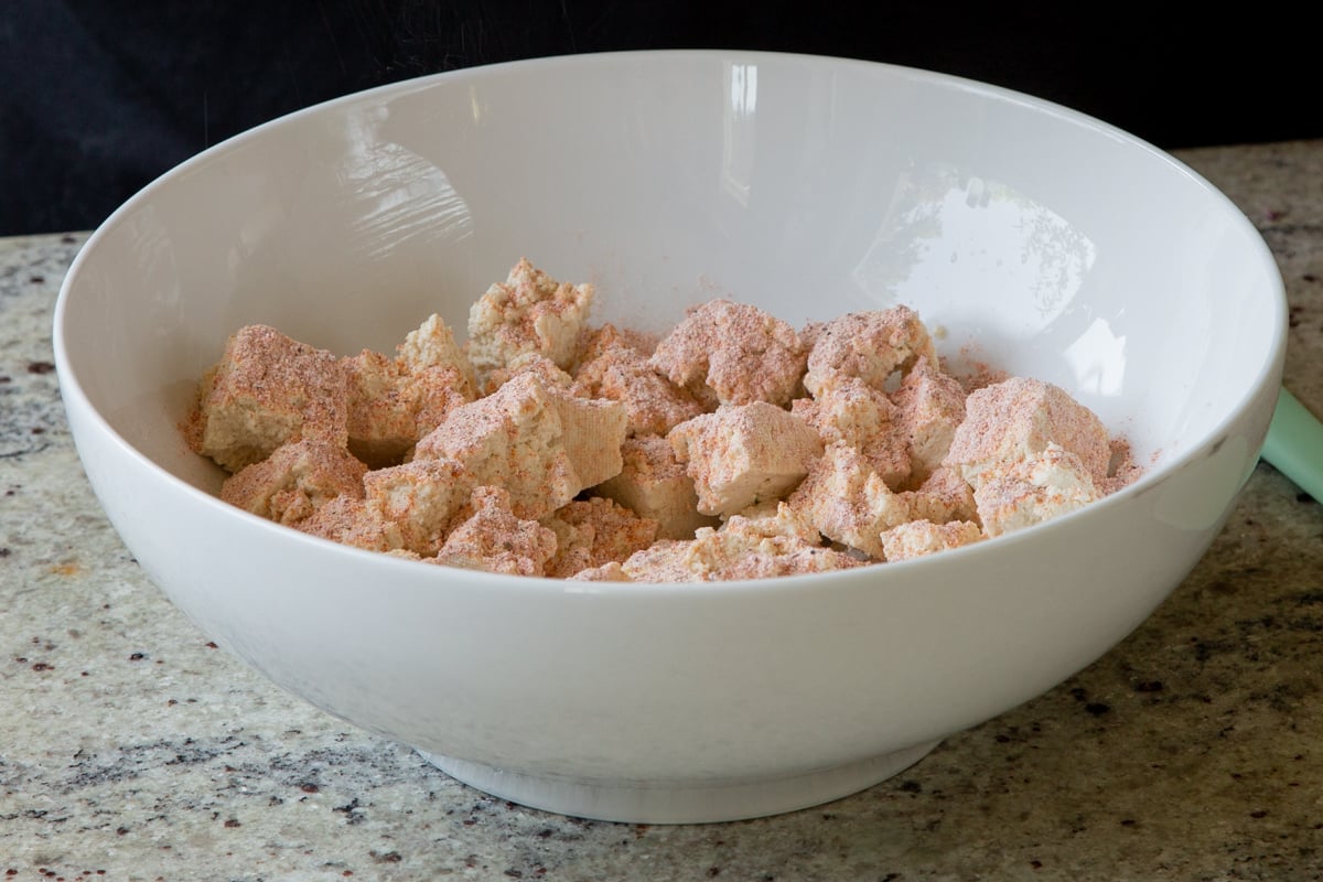 adding spices to torn up tofu in the bowl