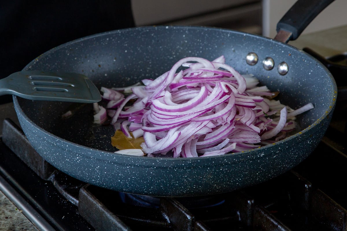 adding onion to the pan of whole spices