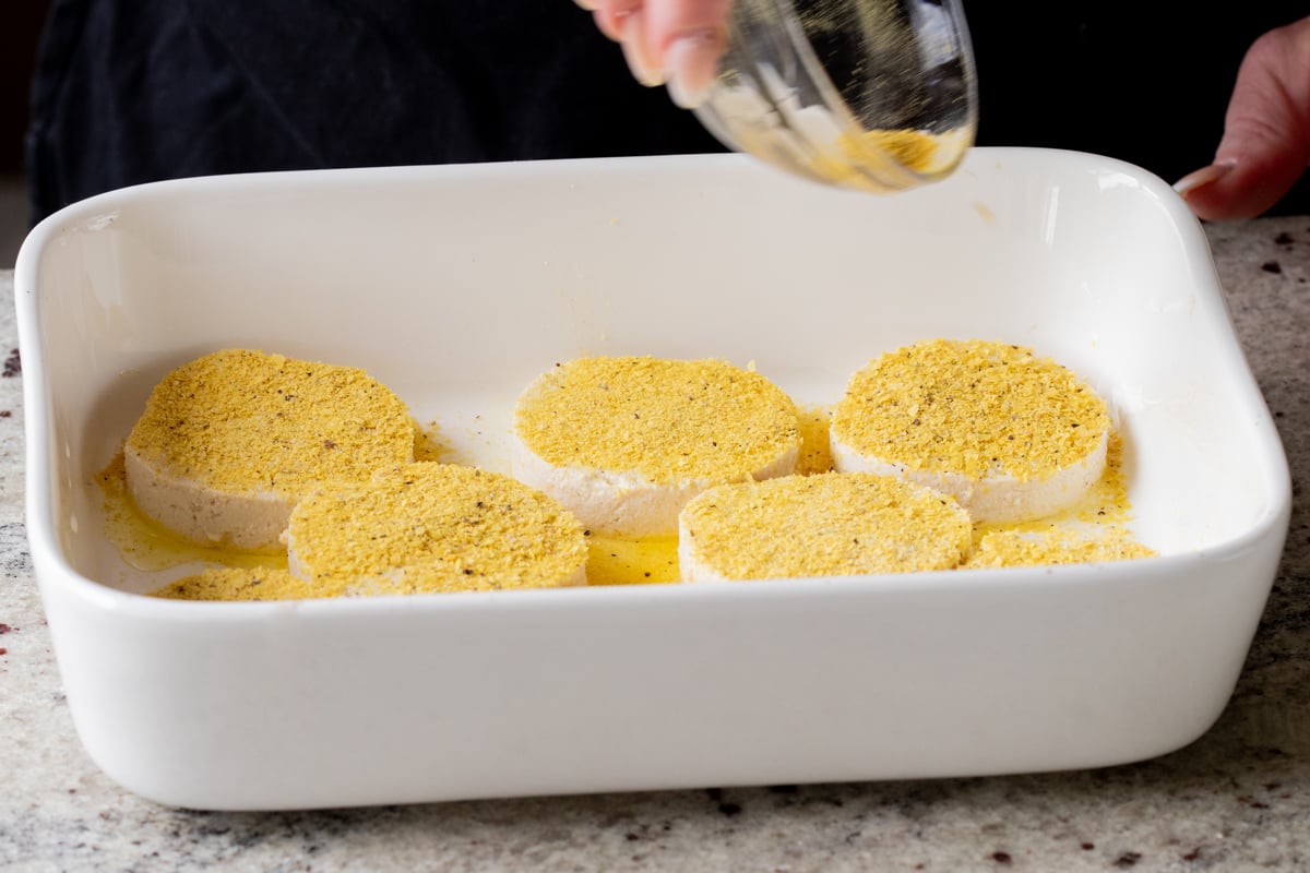 sprinkling seasoning onto the tofu rounds in the greased baking pan